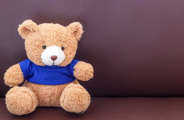 Urso de pelúcia marrom com camisa azul no sofá — Fotografia de Stock