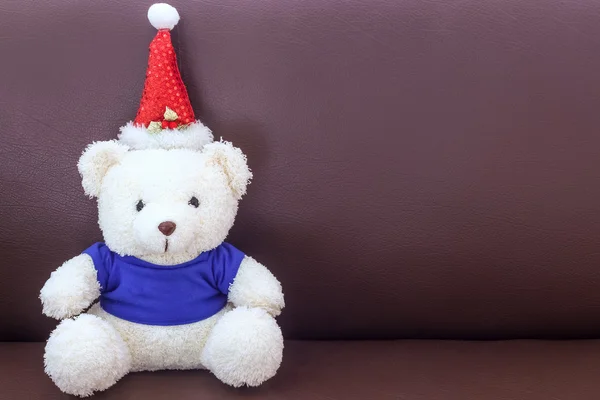 Urso de pelúcia branco com camisa azul usando chapéu de Natal no sofá — Fotografia de Stock