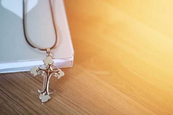 Cross pendant over the book on wooden floor with light flare and copy space — Stock Photo, Image
