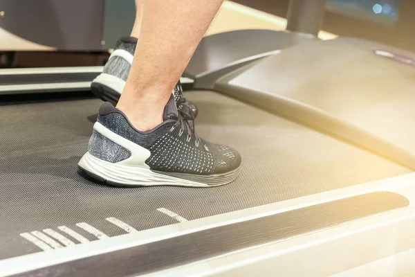 sport, fitness, lifestyle, technology and people concept - close up of men legs walking on treadmills in gym with light flare effect