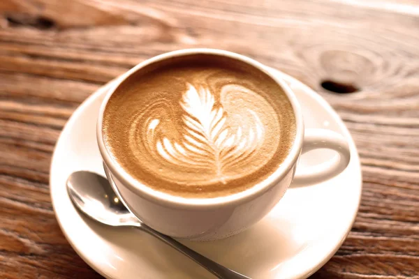 cup of the latte art coffee with spoon and plate on the brown bark beautiful texture background with warm light