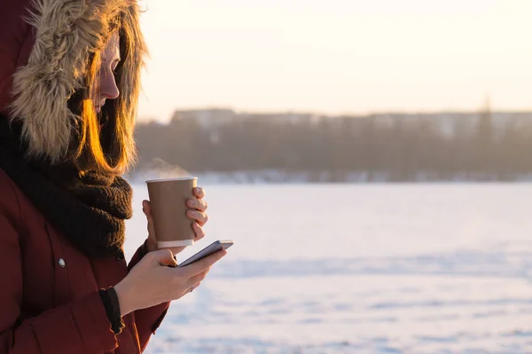 Κρατώντας ζεστά ροφήματα και χρησιμοποιώντας smartphone σε εξωτερικούς χώρους το χειμώνα — Φωτογραφία Αρχείου