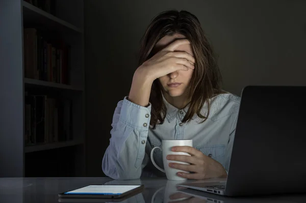 Tired and disappointed female person at home office workplace late at night Stock Picture