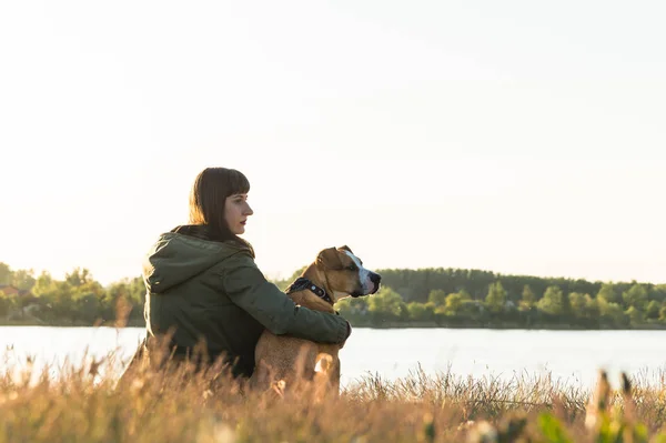 Dono do cão e seu animal de estimação sentar na margem do rio ao pôr do sol — Fotografia de Stock