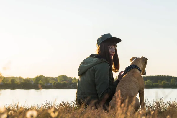 Chica y su perro junto al lago al atardecer — Foto de Stock