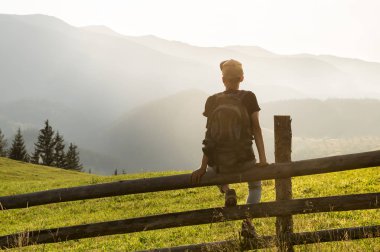 Genç erkek turist wih sırt çantası çit dağların güzel manzara keyfini tepe tarafında oturur