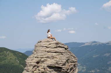 Genç kadın bir kaya dağ kırsal alanda güneşli yaz gününde oturur ve güzel sahne sahiptir