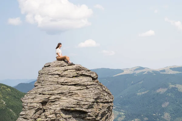 Saçında Rüzgar olan kadın dağ kırsal alanda bir kayaya güneşli yaz gününde oturur ve güzel sahne sahiptir