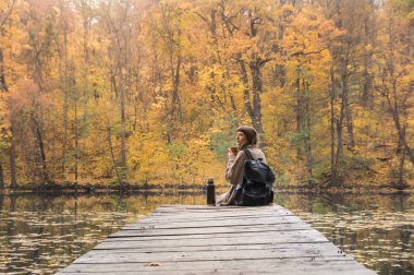 Kız dinlenme sahiptir ve altın sonbahar gününde termos doğa Park lake yakınındaki üzerinden sıcak kahve içer