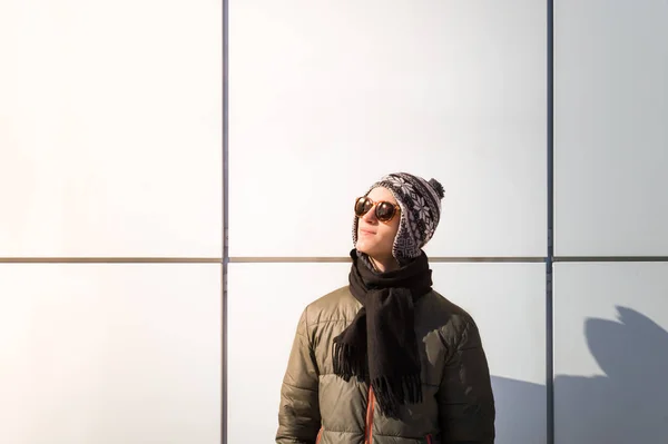 Εφηβικό πρόσωπο θέτει κοντά σε ένα τοίχο σε εξωτερικούς χώρους και κοιτάζει τον ήλιο φωτεινό χειμερινή ημέρα — Φωτογραφία Αρχείου