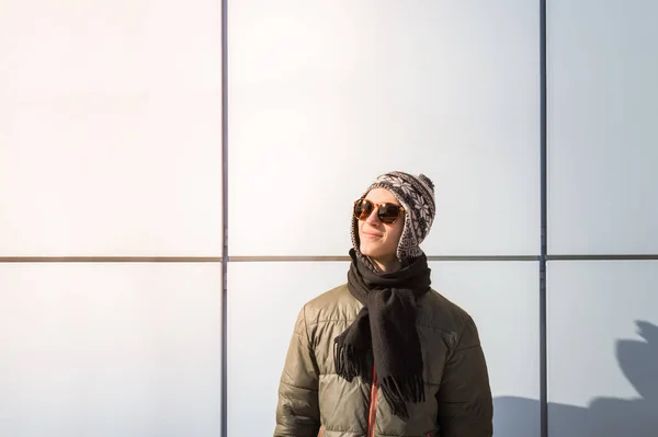 Pria muda bertopi musim dingin dan kacamata hitam dengan latar belakang kota minimalis — Stok Foto