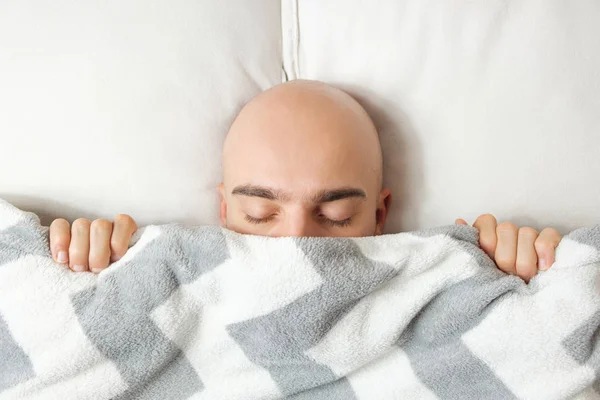 Un jeune homme se couche sous une couverture les yeux fermés et a du mal à se réveiller le matin. . — Photo