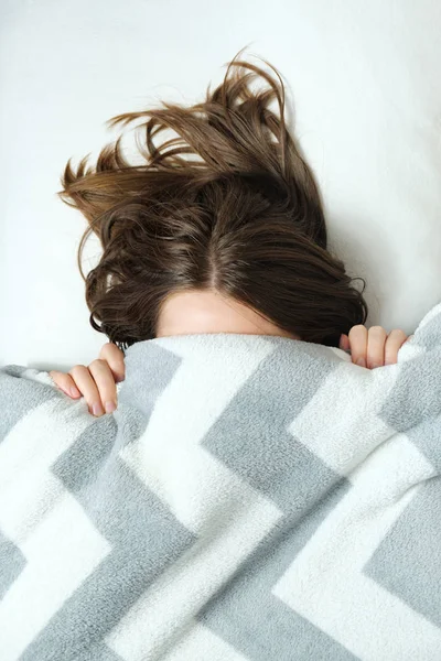 Une jeune femme se couche sous une couverture et a du mal à se réveiller le matin. . — Photo