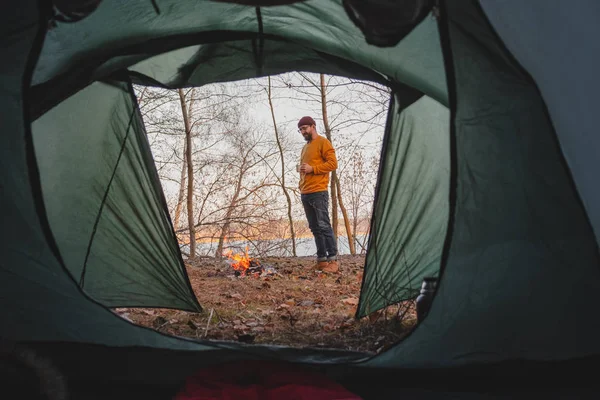 Muž stojící u táboráku a vychutnávající si horký drink. — Stock fotografie