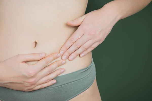 Kvinna som håller händer nära trosor i området reproduktiva organ på grön bakgrund. — Stockfoto