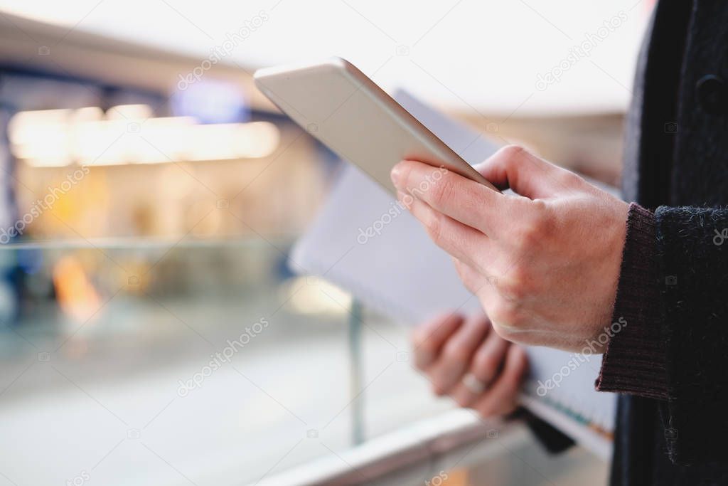 Human hands hold a tablet or e-book at a public place, close-up view. 