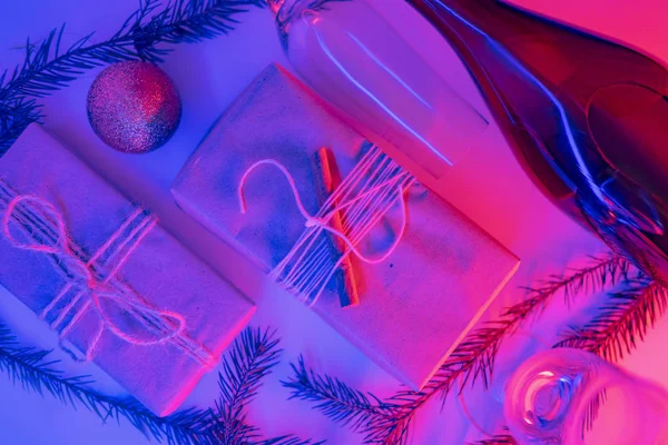 Christmas presents in sustainable package in neon lights. New Year party concept: gifts, beverage and glasses in pink and blue background, top view