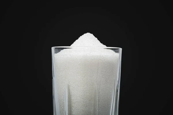 Un vaso lleno de azúcar en fondo negro . — Foto de Stock