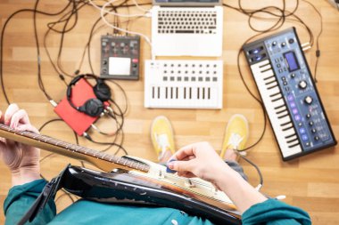 Prova odasında elektro gitar çalan genç bir kadın. Evde gitar ve elektronik enstrümanlar çalan kadın yapımcının en iyi görüntüsü.