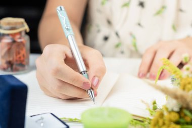 Beyaz defter arkaplanında bir kalem tutan kadın eller