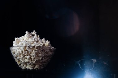 Bir kase patlamış mısır ve siyah arka planda 3 boyutlu sinema gözlüğü. Sinema, 3 boyutlu filmler konsept aperatifler, 3 boyutlu gözlükler ve projektör lambadan çıkan parlak bir ışık.