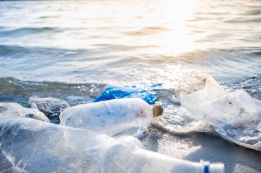 Plajda boş plastik şişeler, deniz kıyısı ve su kirliliği kavramı. Çöp (boş içecek paketleri) deniz kenarına atılır, doğrudan güneş ışığı altında yakın çekim görüntüsü