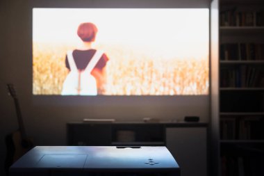 Ev sineması: odadaki bir video projektöründen film izlemek. Oturma odasının duvarında sinematik bir resim var.