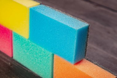 Koyu arkaplanda farklı renkte süngerler bir duvar oluşturuyor. Koyu arkaplanda tuğla gibi duran bulaşık bezi parçaları.