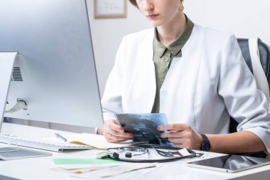 Modern tıp muayenehanesinde kadın hekim. Masaüstü bilgisayarının önünde X-ray 'i inceleyen kadın