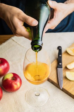Birinci sınıf bir adamın bardağa prim dökerkenki görüntüsü. Erkek ellerinin, olgun elmalarla dolu kırsal masa arka planında güzel bir bardağa kaliteli elma şarabı dökerken yakın plan çekimi.