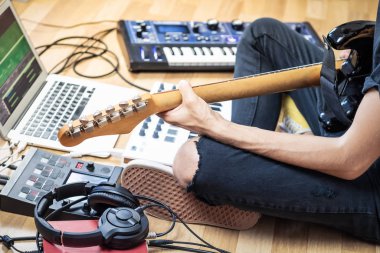 Modern ev stüdyosunda ya da prova odasında elektro gitar çalan erkek gitarist. Elektronik efekt işlemcileri, sentezleyici ve dizüstü bilgisayarlı müzik üreten genç adam