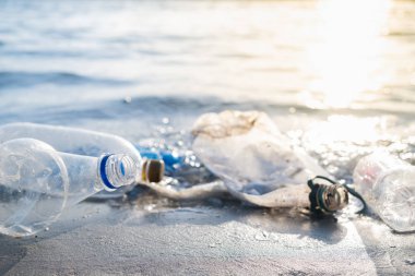 Plajda boş plastik şişeler, deniz kıyısı ve su kirliliği kavramı. Çöp (boş içecek paketleri) deniz kenarına atılır, doğrudan güneş ışığı altında yakın çekim görüntüsü