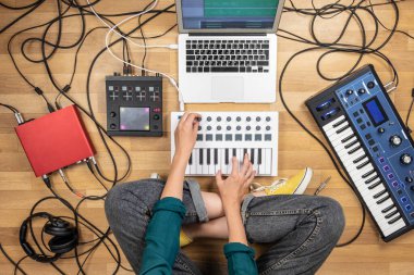 Dizüstü bilgisayar ve dijital aletlerle elektronik müzik yapan bir kadın. Genç bir kadının sentezleyici ve dijital denetleyiciler üzerine modern bağımsız müzik yapmasının en iyi görüntüsü