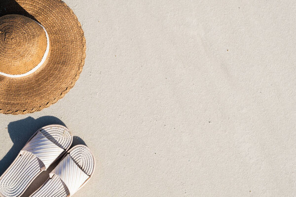 Summer vacation concept: beach slippers and a hat on clean sand. Top view of acessories for seaside holidays with natural copy space resembling seashore