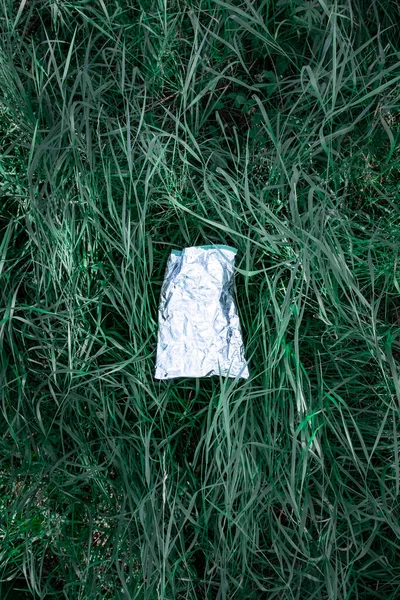 緑の草の中にビニール袋 自然汚染の概念 芝生の上に捨てられたプラスチックごみ 空の食品包装 の欠片 — ストック写真