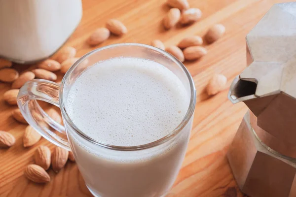 Glass of almond milk and coffee brewer on wood table. Vegan almond drink and moka espresso maker - plant based substitutes for coffee making