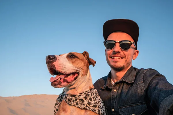 Human taking a selfie with dog on sandy beach. Happy young male person makes self portrait with his dog outdoors