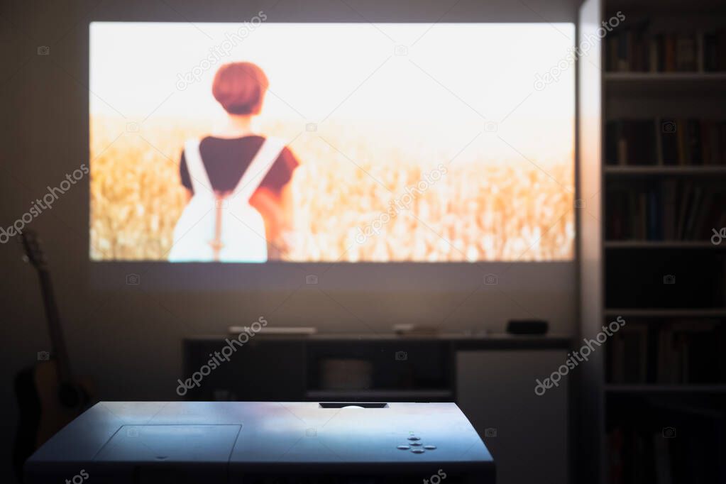 Home cinema: watching a film from a video projector in a room. Dim living room with a cinematic picture projected on the wall