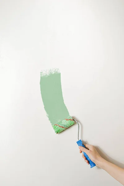 Hand with a paintbrush against the white wall.