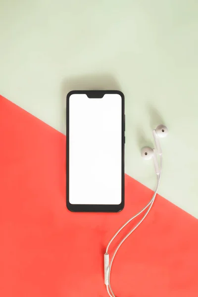 Smartphone moderno com tela branca e fones de ouvido em fundo vívido . — Fotografia de Stock