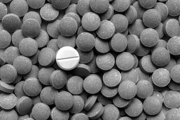 一堆深色药丸围绕着一个白色的 低调的单色 自我治疗或安慰剂概念 一种药片不同于其他许多药片 — 图库照片