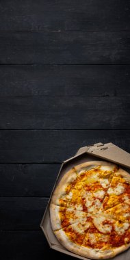 Açık bir teslimat kutusunda pizza margherita, mesaj alanı olan karanlık bir fon. Teslimat yemekleri, paket yiyecek konsepti: siyah ahşap arka plandaki pizza kutuları