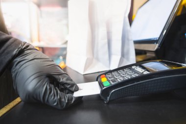 Ödeme için kredi kartını kullanarak, yakın çekim. İnsan eli, bir kasiyer masasındaki POS terminaline ait bir ödeme kartını tutuyor.