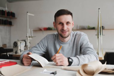 Gülümseyen adam mühendislik yapıyor ya da genel bir atölyede çalışıyor. Yerel küçük işletme, giyim tasarımcısı portresi