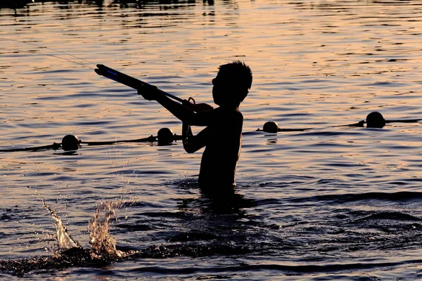 Sunset silhouette of happy child enjoys water games in the swimming pool — Stock Photo, Image