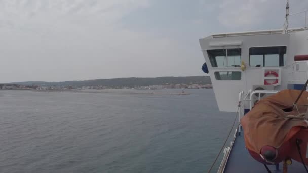 フェリーは穏やかな海でサンピエトロ島に向かい 港の防波堤と赤い灯台 遠くに都市のスカイライン — ストック動画