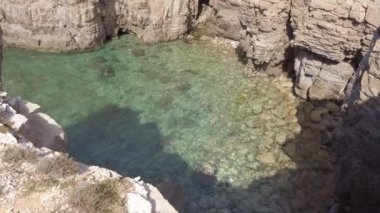 Yukardan bakıldığında kayalık bir körfezin üzerinde zümrüt deniz suyuyla kaplı bir kayalık.