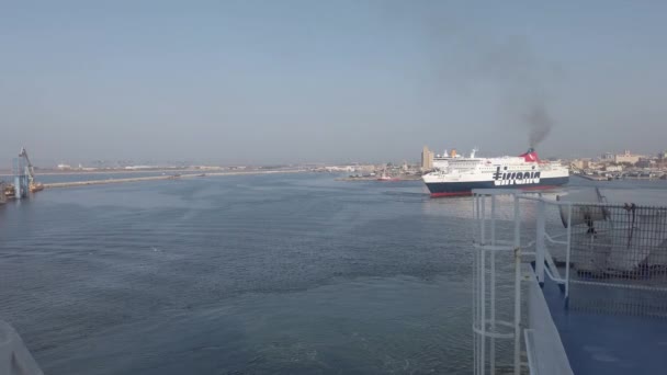 意大利卡利亚里 Cagliari 2019年9月20日 船只接近卡利亚里港的船坞时 海鸥在蓝色海水上空飞行 同时一艘地拉那渡船驶出 码头附近的港口天际线和基础设施景观 — 图库视频影像