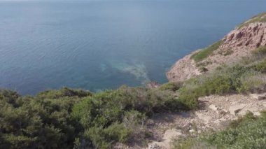 Sardinya bölgesindeki Saint Peter Adası 'ndaki Akdeniz vahşi doğası. Mavi denizin üzerindeki büyük kayalıklar ve zamanın aşındırdığı antik taş blokları arasında yemyeşil bitki örtüsü. İtalya.