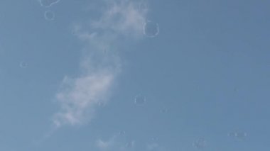 Kaygısız sabun baloncuklarının yavaş hareketi açık mavi yaz gökyüzünde rüzgarın rehberliğinde uçuyor.